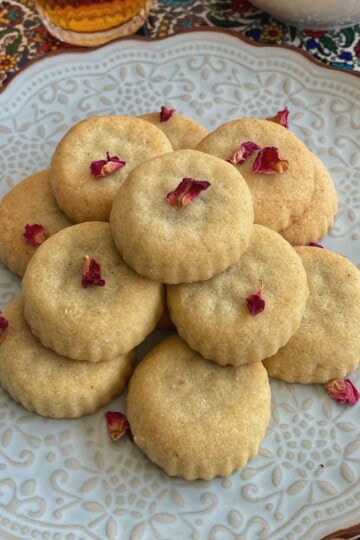 A stack of maamoul in a plate with some dried rose petals garnish.