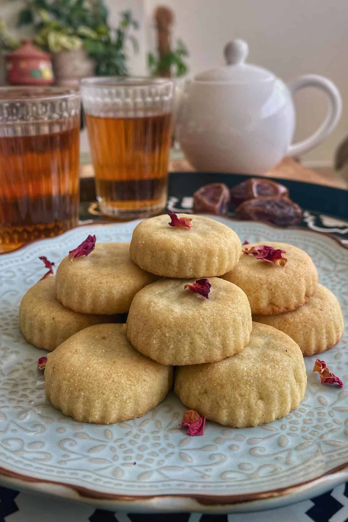 A dessert plate with date stuffed maamoul garnished with dried rose petals served with two black tea.