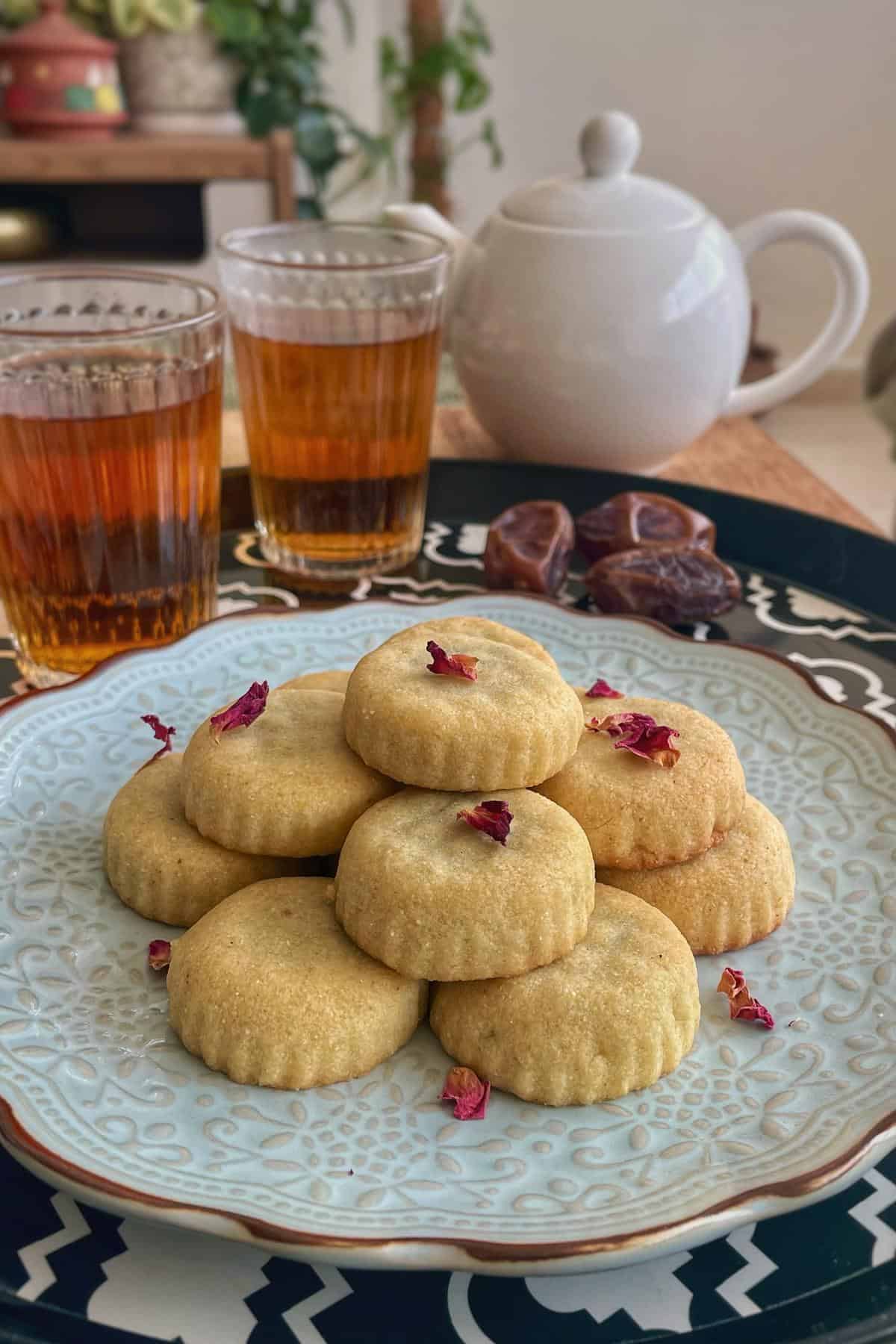 A stack of maamoul date cookies with two glass of black tea and a kettle. 