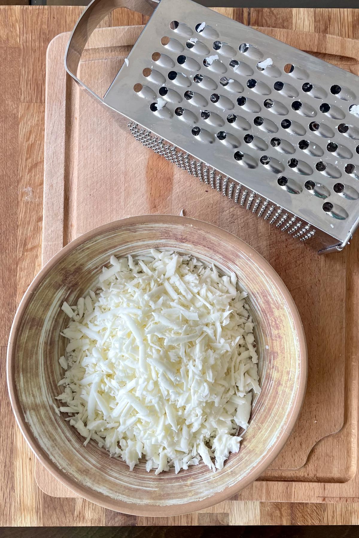 A bowl of grated halloumi using a large hole grater.