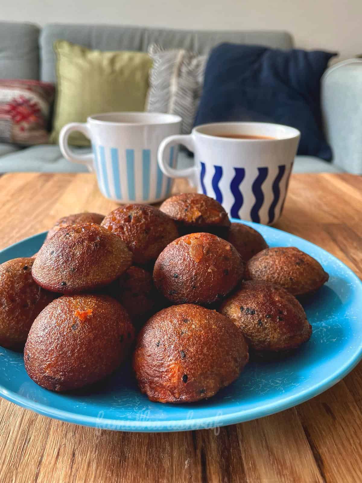 A dessert plate filled with fried unniyappams along with two cups of chai.