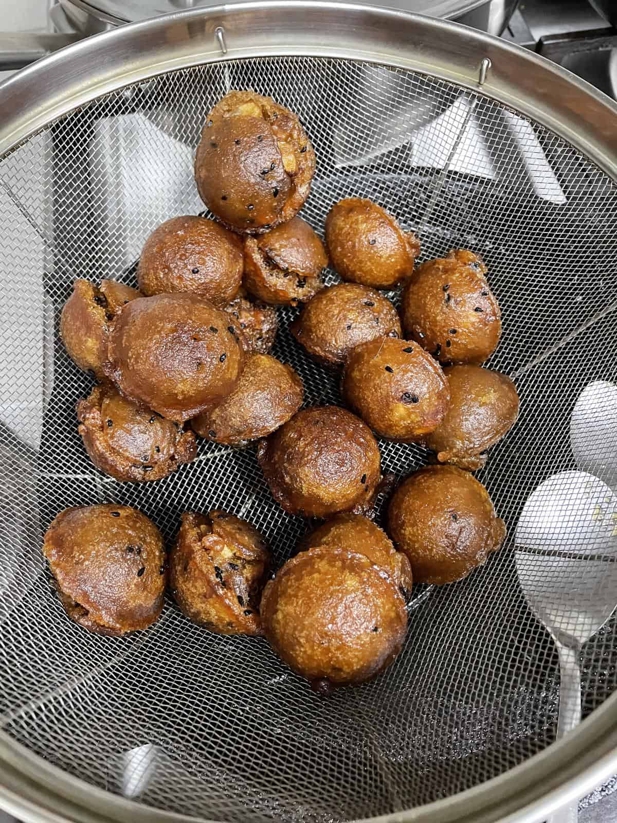 Fried unniyappams in a wire colander.