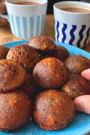 A plate of unniyappams with two cups of chai and my hands reaching for one.