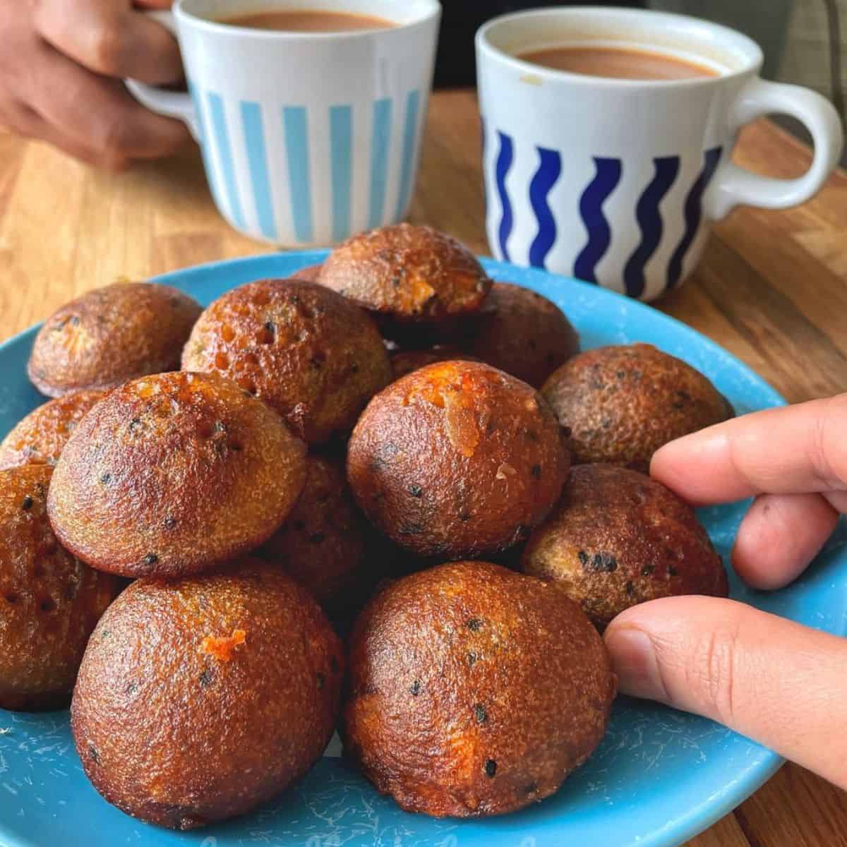 A plate of unniyappams with two cups of chai and my hands reaching for one.